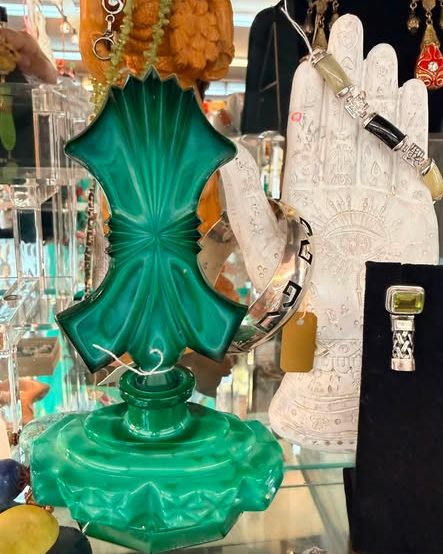 A green malachite glass vase beside a ceramic hand displaying bracelets