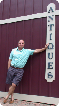 Chris Freiheit leaning against the mall's ANTIQUES sign